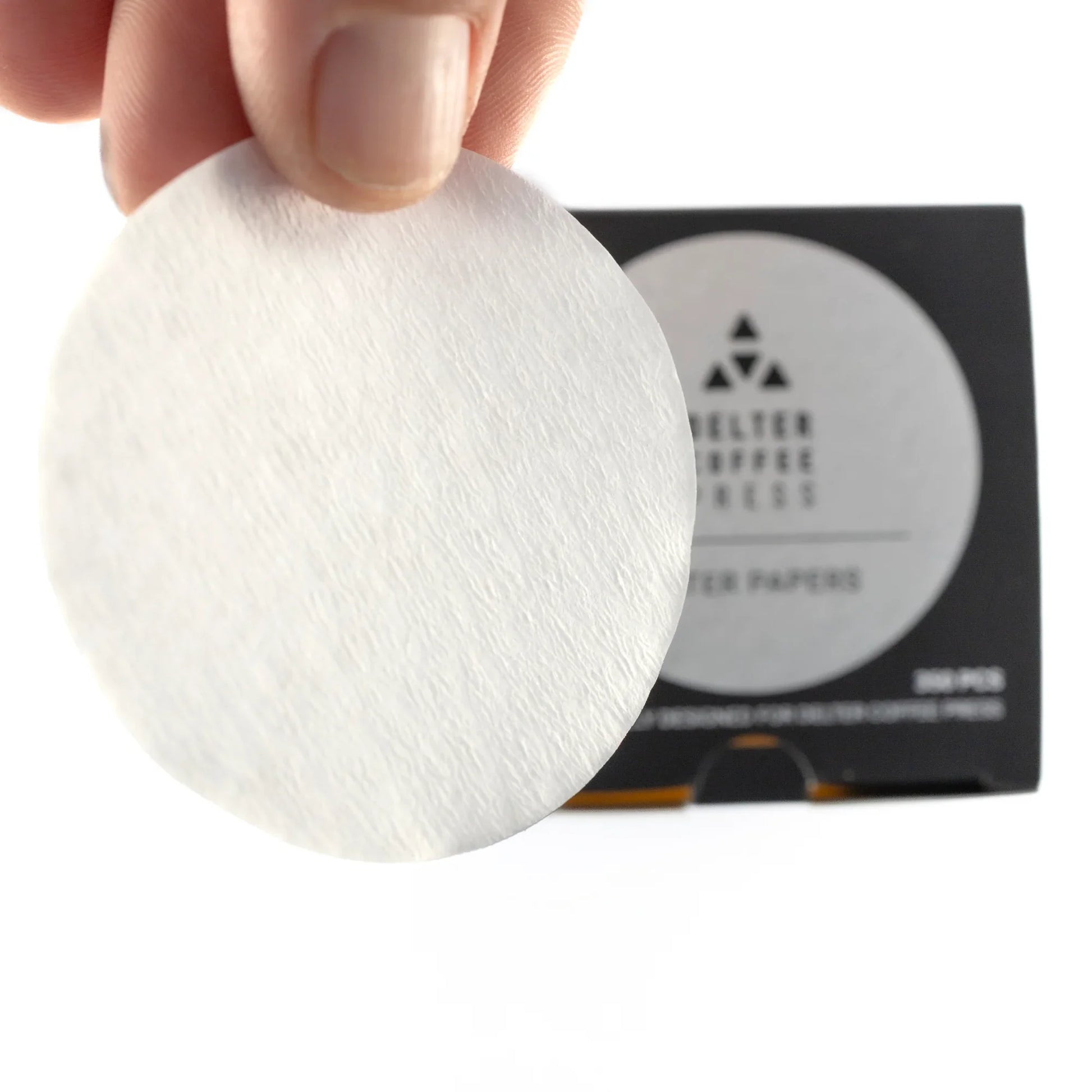 Hand holding round Delter Coffee Press filter paper with branded box in background
